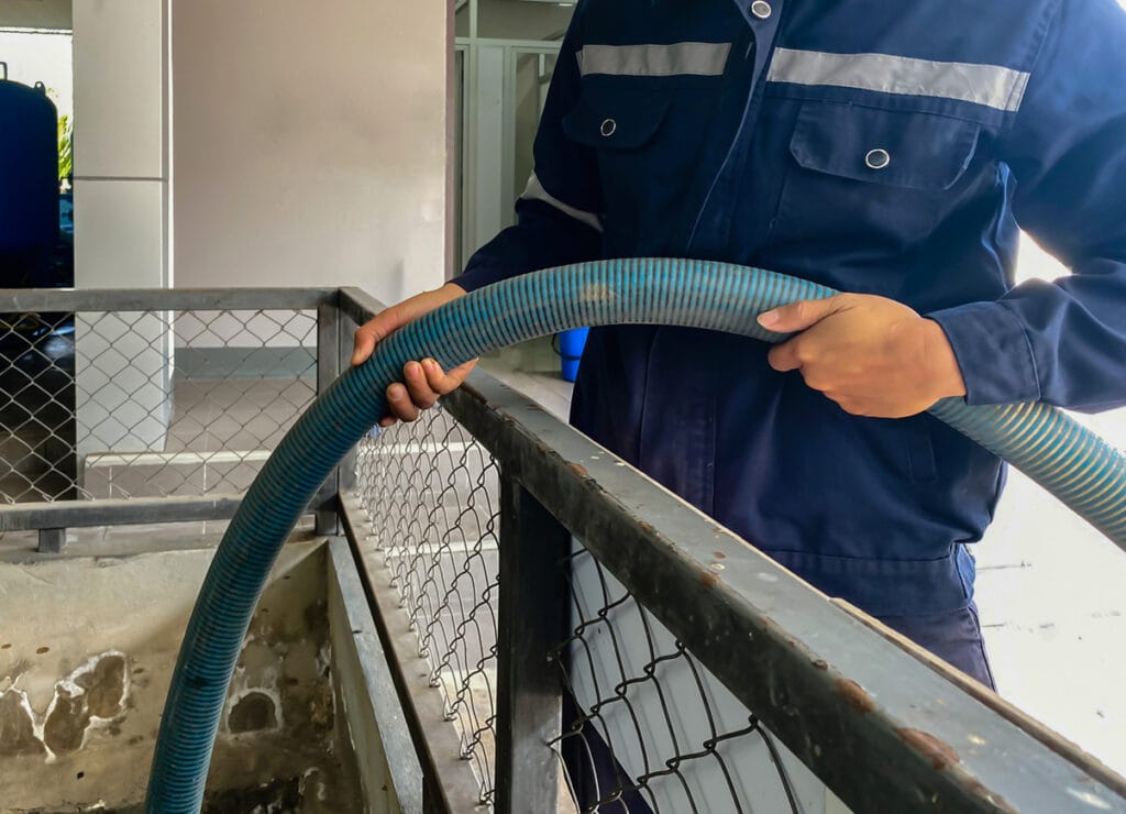 A Worker Wearing Protective Clothing Holding A Hose Is Pumping Sludge Out Of A Concrete Sewage Pond In A Plant